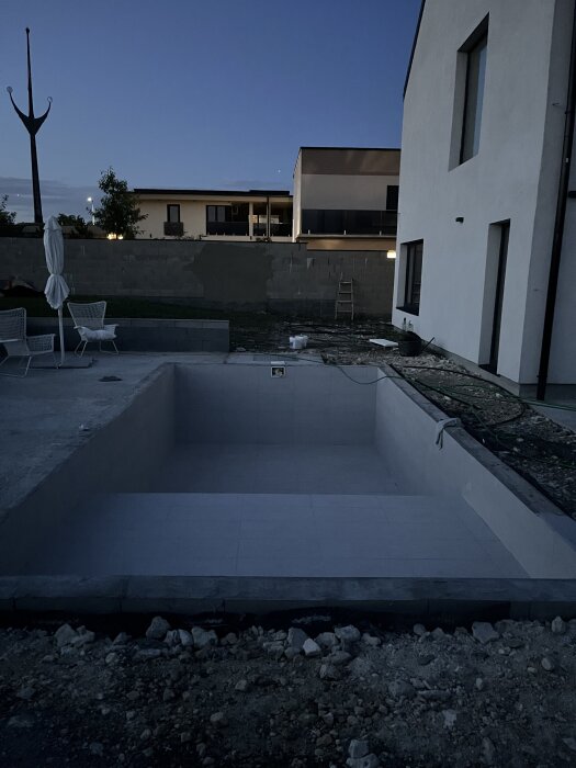 Nedgrävd pool utan vatten, fogad med epoxy, vid ett modernt hus under skymning.