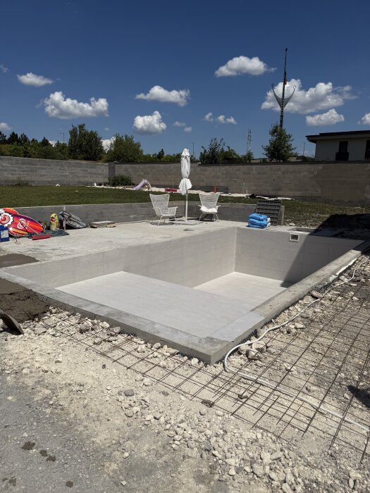 Markarbete runt en odekorerad pool och terrass med stolar och parasoll i bakgrunden. Plattsättningsmaterial syns på marken.