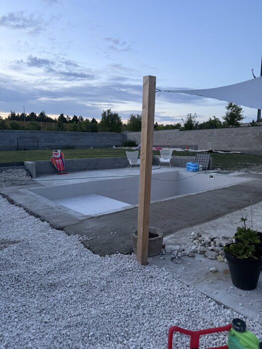 Markarbete pågår runt en pool och terrass, med grus och jord, i förberedelse för plattsättning. Stolar och mål i bakgrunden.