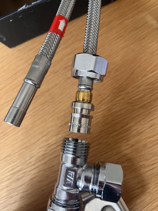 Flexibel metallslang och T-koppling, med en 15x10 förminskning liggande ovanför. Slangen är redo för anslutning till T-kopplingen.