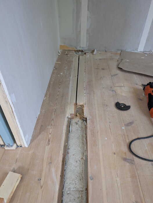 Saknad golvplanka i furugolv, avslöjar isolering underst. Verktyg synliga bredvid.