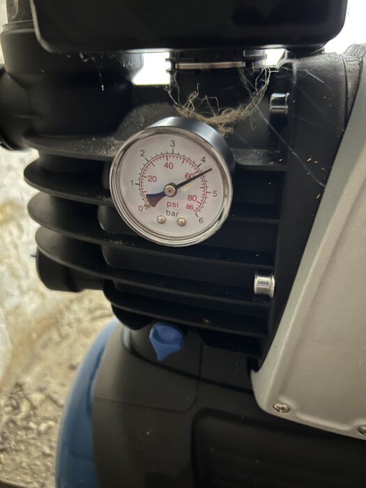 En manometer på en pump, visar ett tryck på över 4 bar, med en bakgrund av damm och skräp.