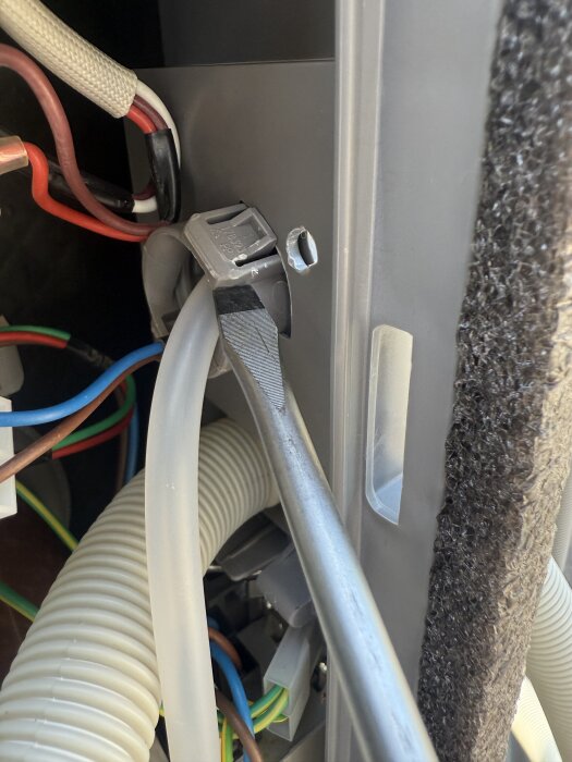 Bild av en slangklämma och elektriska kablar, inklusive en kabel i en klämma, i en maskin eller apparat, med synlig isolering och en skruv.