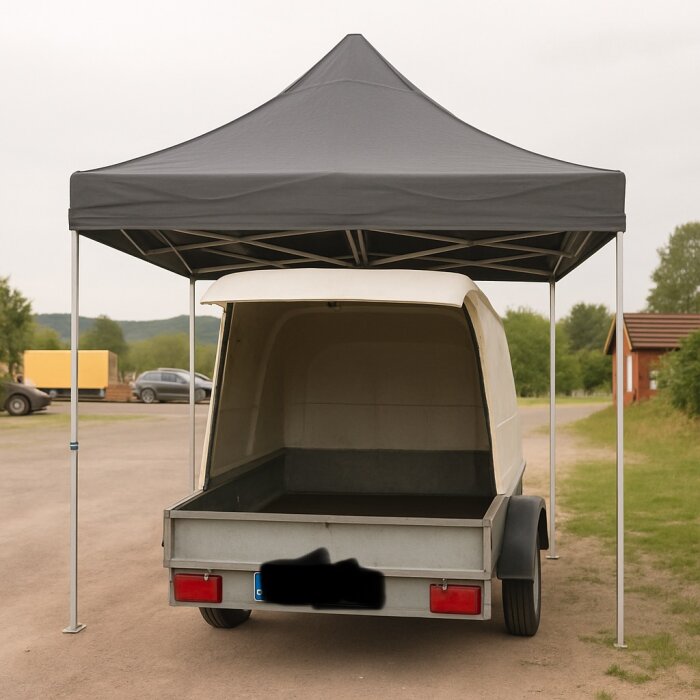 Släpvagn med uppfälld baklucka under svart popup-tält. Tältet sträcker sig väl över släpet för att ge skydd mot väder.