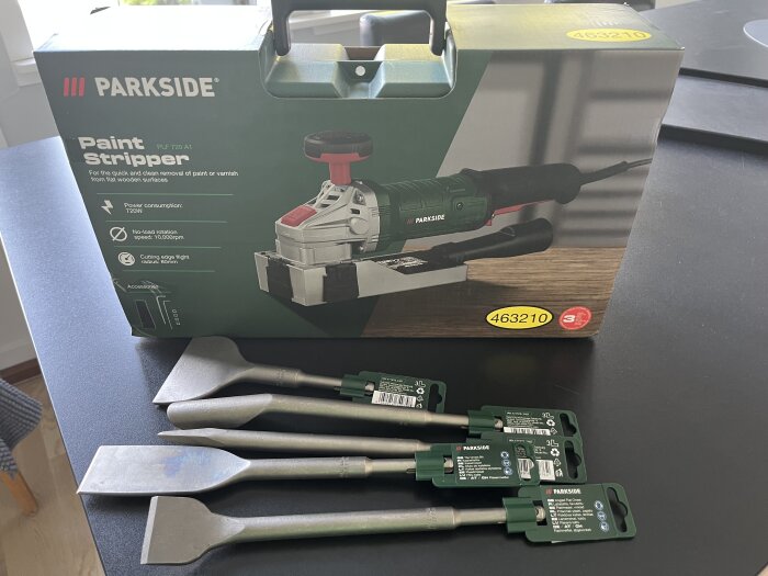 Kartong med Parkside färgborttagare och fyra metallverktyg på bord.