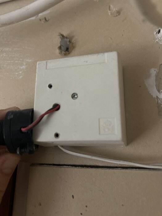 Vit plastlåda med kablar och skruvar, fastsatt på vägg. Användaren frågar om dess funktion.