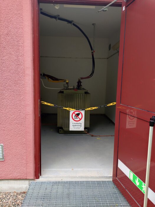 Öppen dörr till transformatorrum med varningsskylt "Livsfarlig spänning", avspärrat med kedja för att hindra obehörig åtkomst.