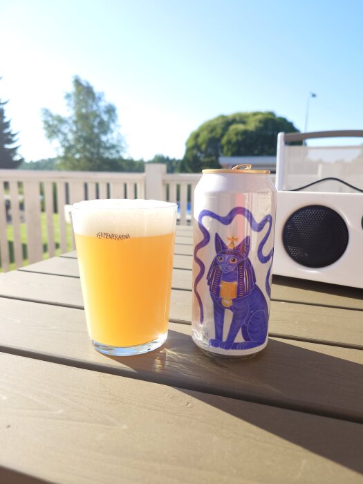Burk och glas med öl från Fermenterarna på ett utomhusbord i solsken.