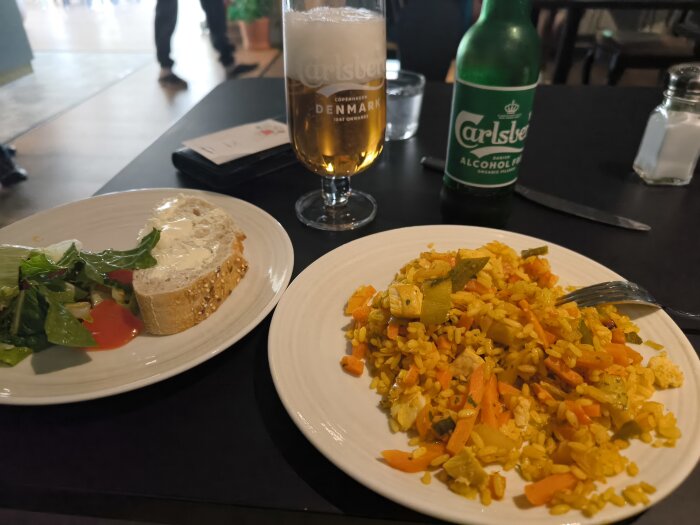 Tallrik med Nasi Goreng, ett glas alkoholfri öl och en brödbit med sallad på ett bord.