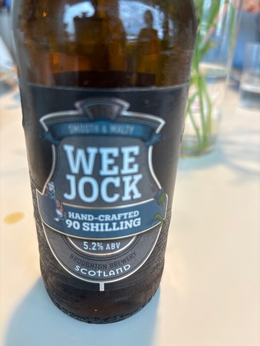 Flaska av Wee Jock öl från Broughton Brewery, 5.2% ABV, med etikett som säger "hand-crafted 90 shilling", placerad på ett bord.