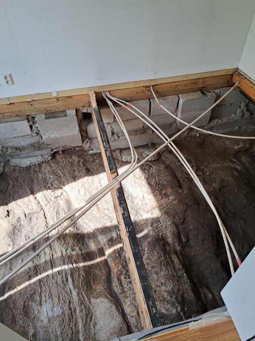 Krypgrund med berggrund, träbalkar och synliga rörinstallationer i ett renoveringsprojekt.