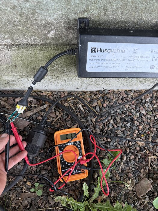 Multimeter visar spänning, ansluten till Husqvarnas strömförsörjning utomhus.