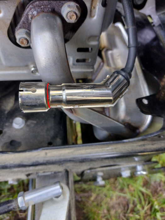 Närbild av en tändstiftskontakt och metallhylsa på en åkklippare, med fokus på den del där gnistproblemet diskuteras.