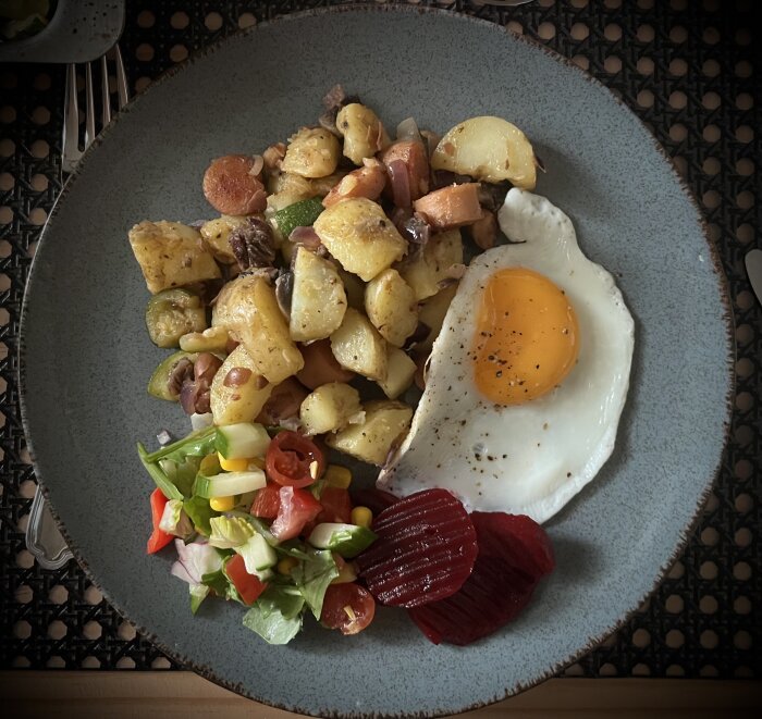 Tallrik med pytt i panna, stekt ägg, sallad och inlagda rödbetor.