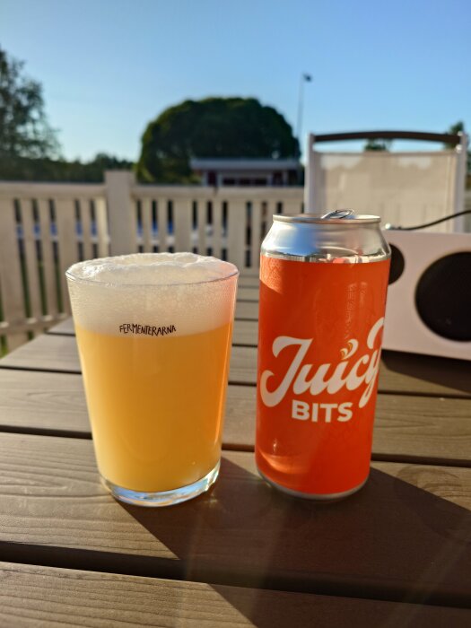 Ett glas öl och en burk med texten "Juicy Bits" på ett bord i solen.
