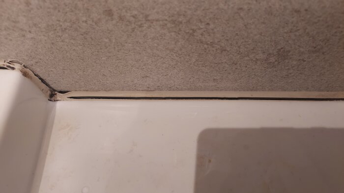 Glipa i fogmassan bakom ett tvättställ, med mörk missfärgning i hörnet och ljusa kalkavlagringar mot väggen.