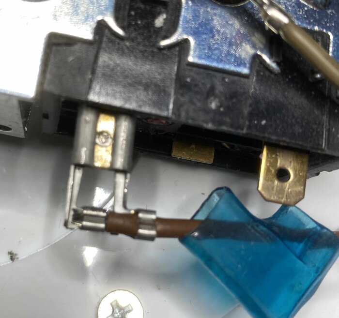 Närbild av en elektrisk komponent i en avfuktare, visar en plugganslutning med blå plastöverdrag och bruna kablar. Skruvhuvud syns i förgrunden.