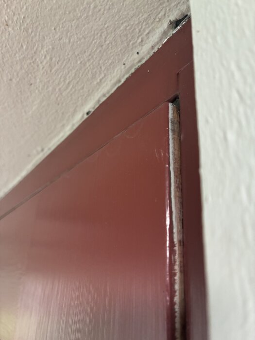 Övre högra hörnet av en trädörr som inte passar perfekt i karmen. Dörren hänger ut något, vilket skapar en glipa.