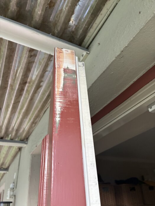 En röd ytterdörr som inte passar exakt in i karmen på grund av skevhet, med en tydlig glipa i övre högra hörnet mot dörrkarmen.