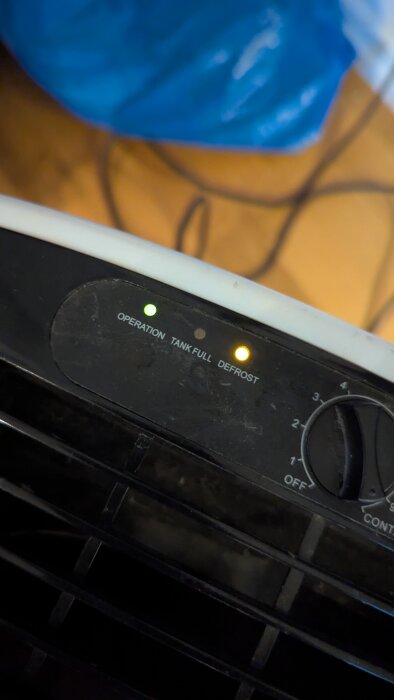 Närbild på kontrollpanel av luftavfuktare med grönt ljus för "Operation" och blinkande gult ljus för "Defrost". Reglage bredvid panelen.