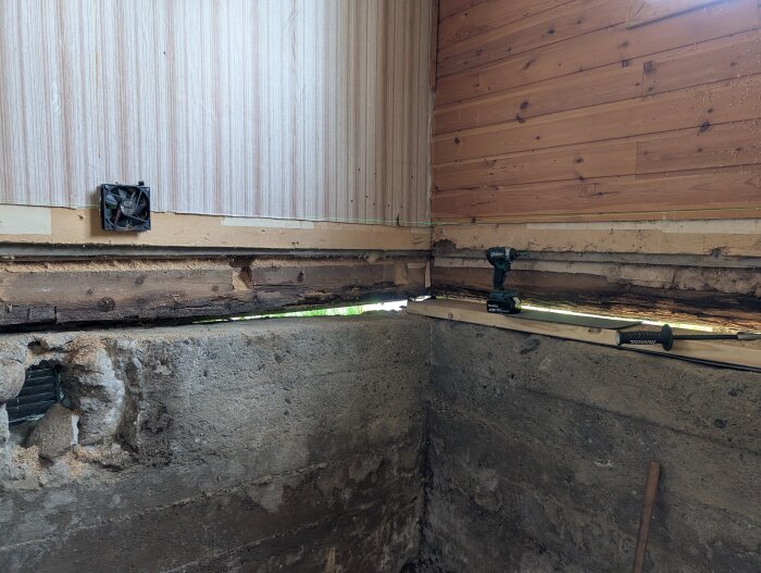 Förstärkta bärlinor och syll i hörnet av ett rum med träpanel på väggar. Inklusive verktyg på golvet och synliga grundmursdetaljer.