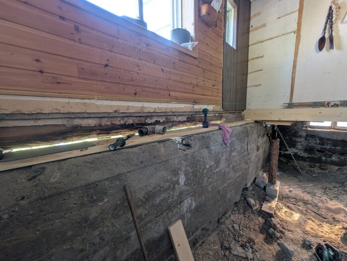 Renovering av husgrund där bärlinan förstärks med reglar och en ny syll monteras på en grundmur. Verktyg och material syns på platsen.