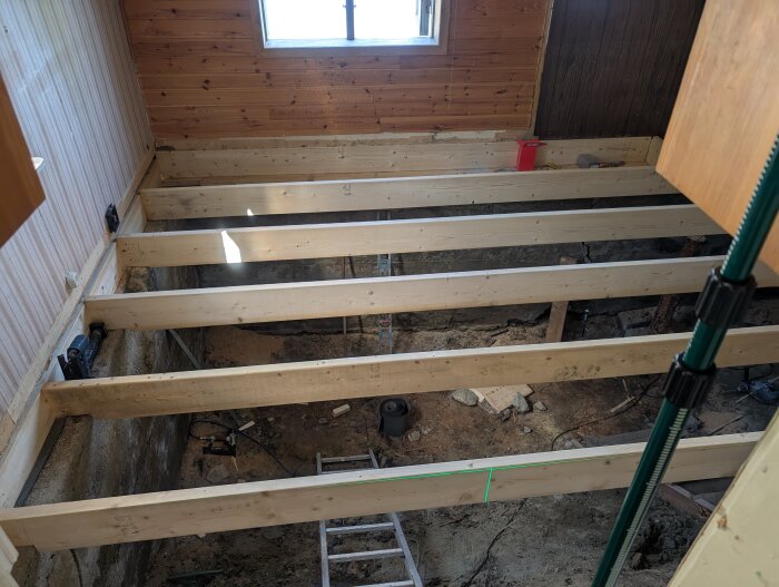 Rummets bjälklag med träreglar, en stege och verktyg på golvet under, under pågående husrenovering.