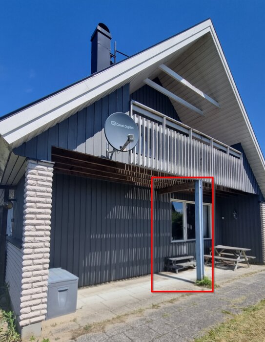 Rödfärgad ruta kring en ruttnande trästolpe vid en husvägg, med en fästplatta intill och en satellitdisk på väggen ovanför.