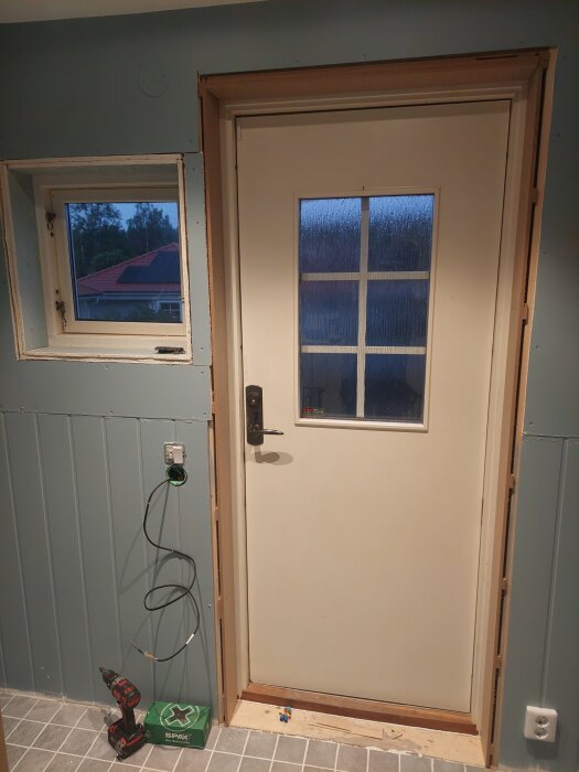 Dörr och fönster med installering av MDF-smygar, borrmaskin och kablar synliga, samt pågående renovering i ett rum med trägolv.