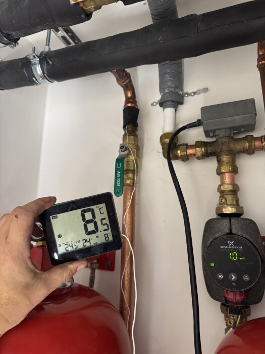 Manuellt mätinstrument visar 8,5 grader vid kylsystem med kopparrör och pumpar, del av frikylinstallation.