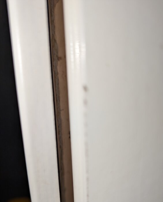 Närbild av en dörrkarm som visar en smal springa mellan dörr och karm, eventuellt med fuktskador från vattenstänk.