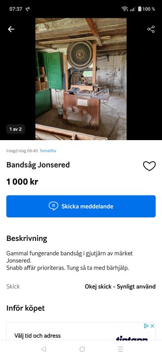 Gammal bandsåg i träverkstad med verktyg på arbetsbänk, omgiven av gröna skåp och trätak.