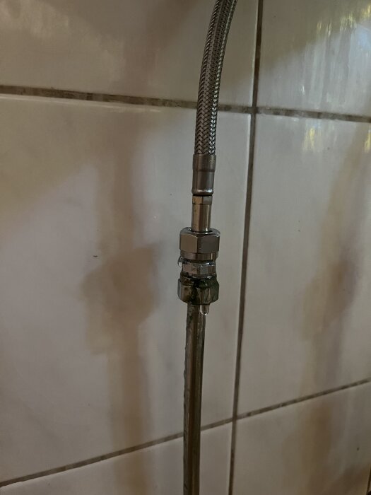 Koppling med läckage på slang i badrum, två muttrar synliga.