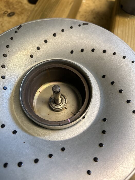 Metallbricka med fastnat lager och stång, omgiven av perforerade hål; del av en diskussion om byggproblem.