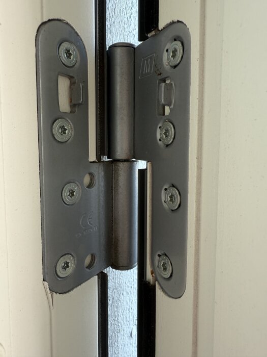 Gångjärn på altandörr, närbild visar flera skruvar och saknad justermån, del av problemet med att dörren skrapar i underkant.