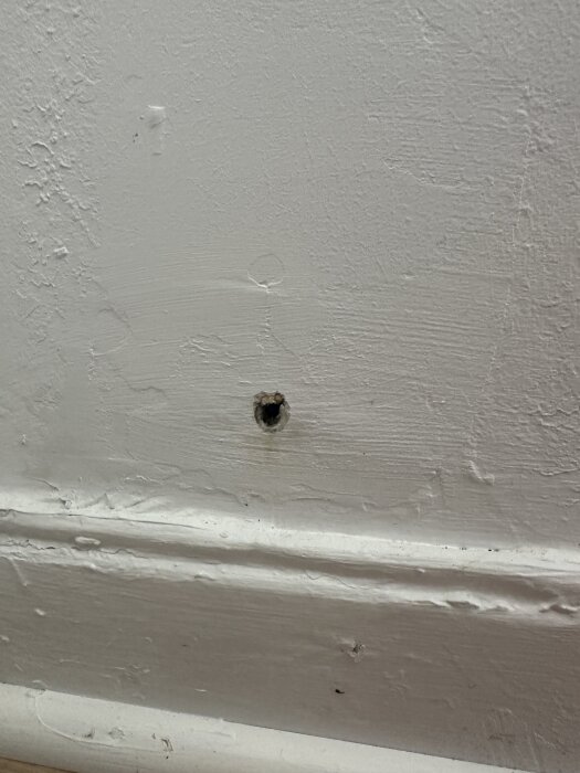 Hål i vit vägg med kraterliknande spricka runtom; kan vara skada från tidigare blixtnedslag.