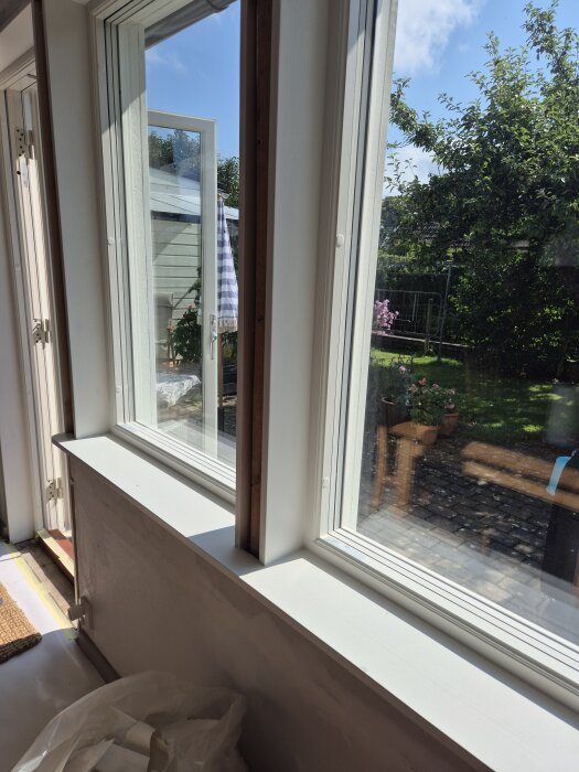 Nymålade fönsterbrädor av furu, inuti ett rum. Soligt väder utanför, med öppet fönster mot en trädgård.