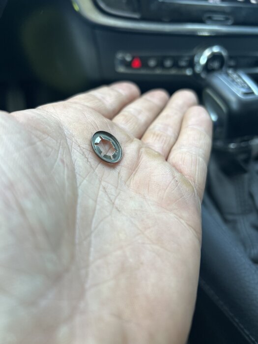 En tandad metallbricka med falsad kant ligger i en hand, fotograferad i en bilinteriör.