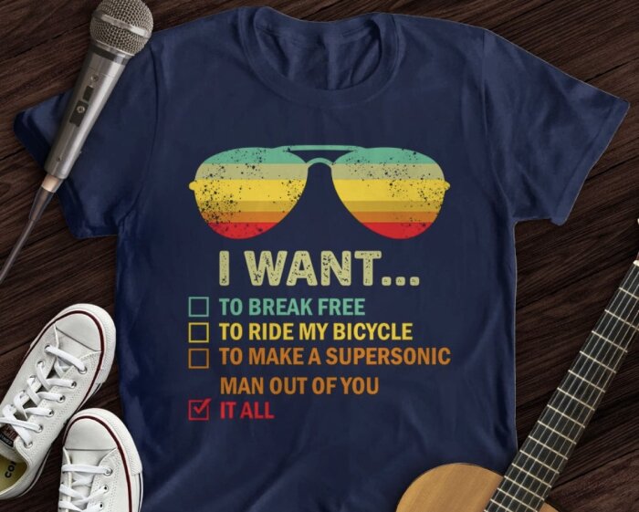 Blå t-shirt med retro-solglasögon och texten "I WANT... TO BREAK FREE, TO RIDE MY BICYCLE, TO MAKE A SUPERSONIC MAN OUT OF YOU" där "IT ALL" är ikryssat.