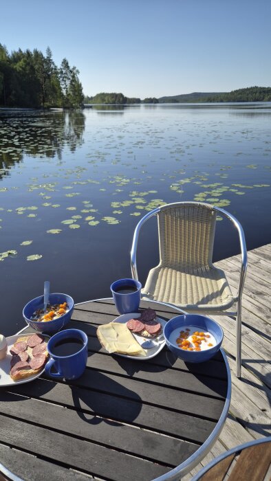 Frukost på bryggan med yoghurt och hjortron, knäckebröd med korv, ostmacka, te och sjöutsikt i Dalarna.