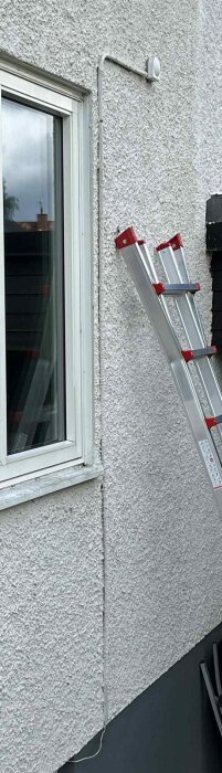 Fasad med kabel som går från fjärrvärmecentralens utomhussensor till en dosa, liknande gammaldags telefonsladd. Stege intill fönster.