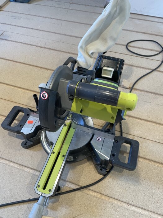 En kap- och geringssåg med batteriadapter står på ett trägolv, används för att såga mindre reglar.
