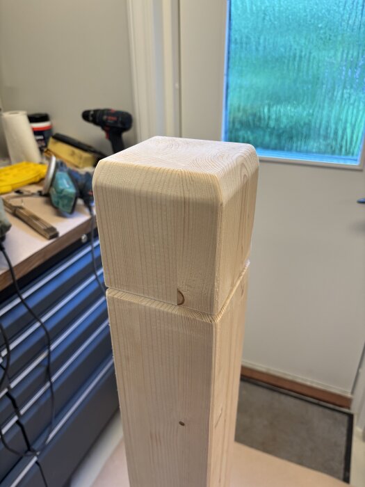 Rundad trästolpe med slipat hörn, skapad med vinkeljärn och slipverktyg i verkstadsmiljö.