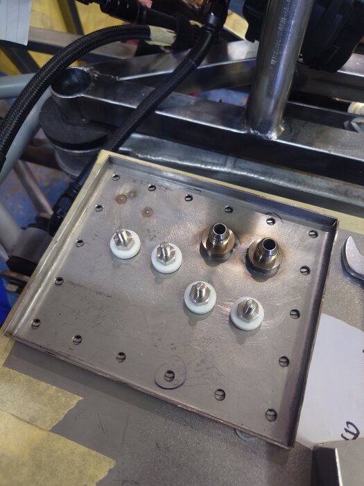 Metallplatta med flera monterade genomföringar och beslag, omgiven av kablar och rör.