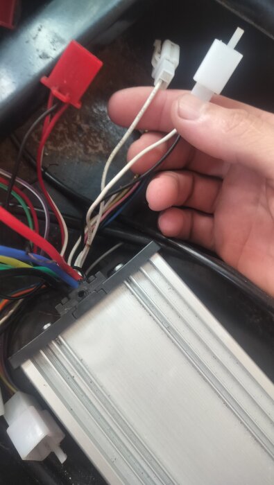 En hand håller i vita kablar och kontakter vid sidan av en rad färgade kablar och en metallisk komponent.