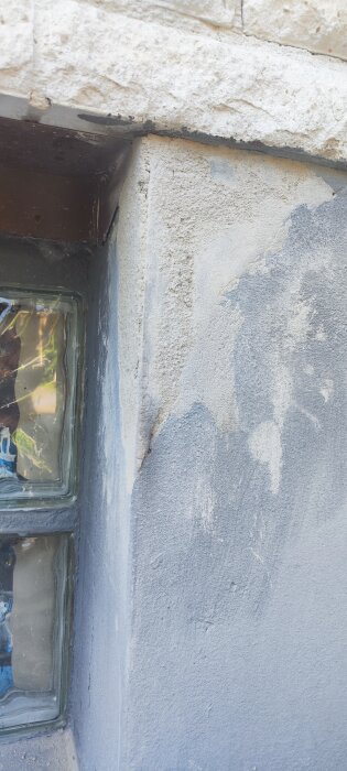 Sprucket hörn på husets sockel med ojämn murbruk och små sprickor, intill glasblocksfönster.