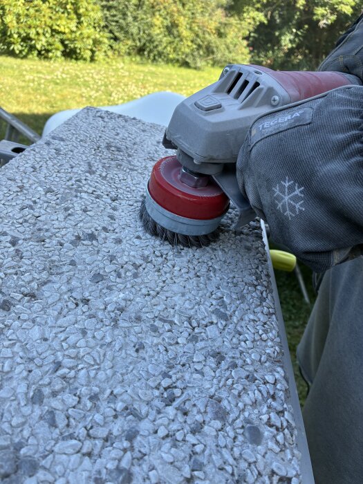 Vinkelslip med metallborste rengör gammal sjösten utomhus i trädgårdsmiljö.