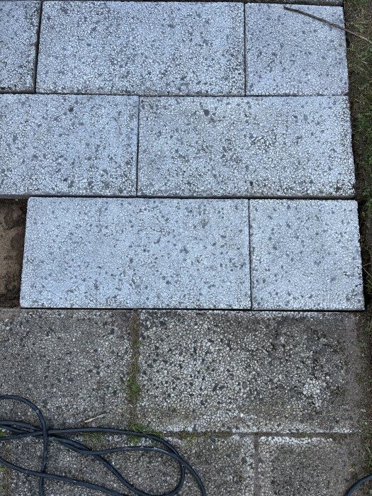 Rengjord dansk sjösten med tydlig kontrast mellan nytvättad och smutsig yta, omgiven av gräs och en elkabel liggande över stenen.