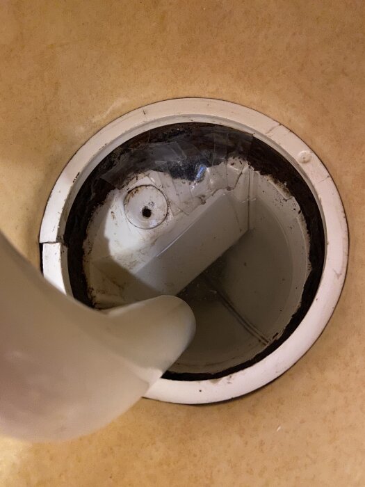 Golvbrunn i badrum utan vattenlås, märke Purus P 50, med ett rör inuti mot brunnen mot en beige bakgrund.