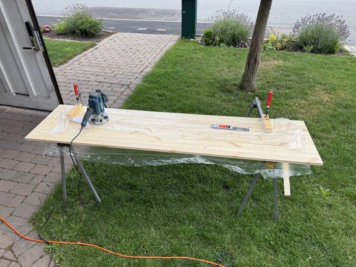 Träskiva på bockar med överhandsfräs, nivåmätare och klämmor i trädgården, förbereds för fräsning.